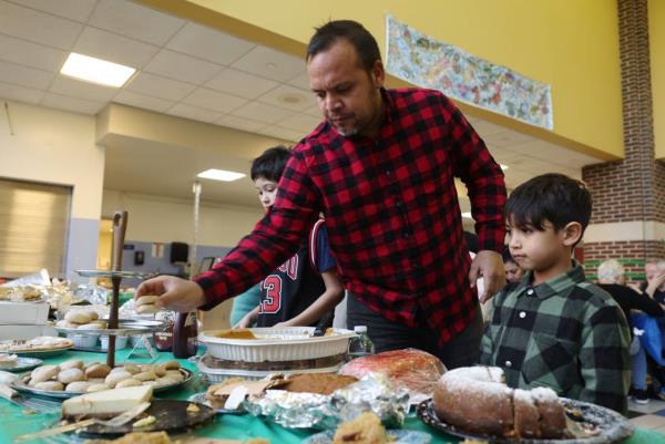 Pablo Lopez reaches for traditional Venezuelan cookies called polvorosas to give to his son Paul, 6, during a potluck Thanksgiving dinner with students, teachers and parents at Chappell Elementary School in Chicago on Nov. 22, 2023. 
